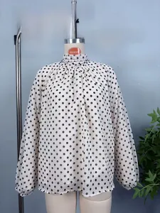 Detail von Stehkragenfalten und schwarzem Punktemuster auf cremefarbener Chiffonbluse