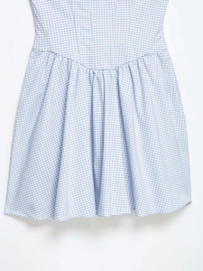 Détails d'une robe vichy bleu et blanc avec coupe cintrée et finitions plissées élégantes