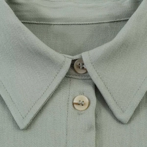 Detail shot of a light grey-green shirt collar featuring a standard pointed lapel and buttons
