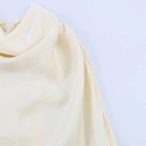 Detail of a creamy white satin dress featuring a draped halter neckline and silky fabric