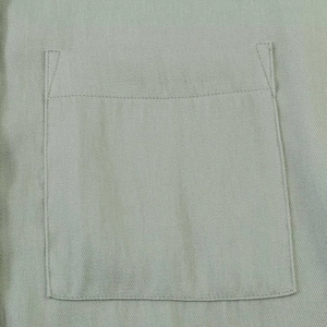 Close-up of a square patch pocket on light green twill fabric with fine stitching detail