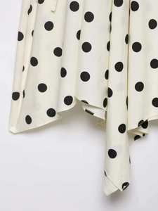 Close-up of ivory fabric with black polka dots and asymmetrical ruffled hemline