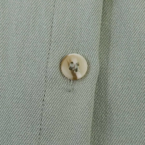 Macro shot of a sage green shirt detail featuring a marble-textured button and twill fabric