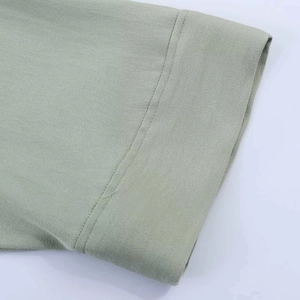 Close-up of double-stitched hem and textured light sage green fabric on shirt