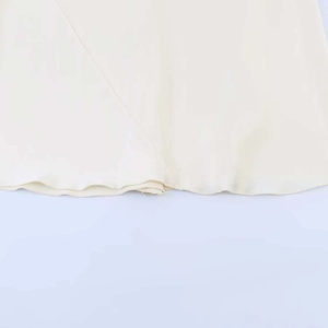 Detail showing the hem stitching and smooth silk texture of the beige halter dress