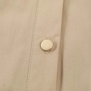 Détail d'une robe en coton kaki clair présentant un bouton en métal doré clair poli