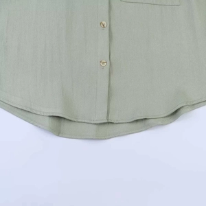 Detail of light green linen shirt with wood texture buttons and curved hemline