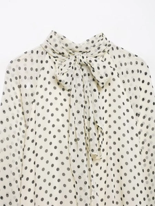 Detail der weißen Langarmbluse mit schwarzen Punkten und elegantem Schleifenausschnitt