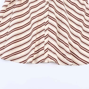 Detail of elegant striped midi dress hem with brown and beige patterns and round button