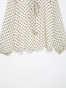 Detailaufnahme der weißen Chiffonbluse mit schwarzen Punkten, Schleife und Gummibündchen
