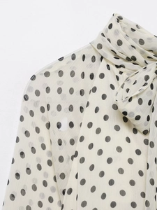 Detail der eleganten Schleife am Ausschnitt der cremefarbenen Polka-Dot-Bluse