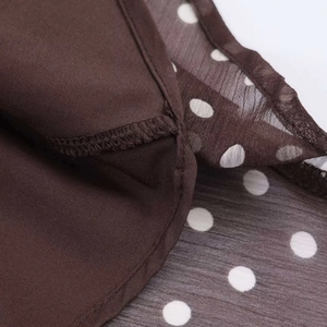 Detail shot of brown polka dot chiffon fabric showing high-quality overlock stitching edges