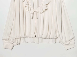 Detail der cremefarbenen Satinbluse mit Rüschen, V-Ausschnitt und Kordelzug mit Goldspitzen