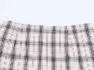 Detail of plaid asymmetric skirt featuring neutral beige tones and precise stitching details