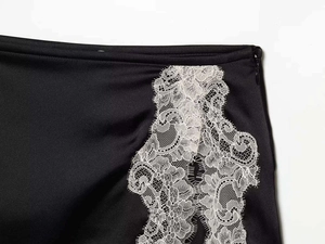 Détail d'une jupe en satin noir avec fermeture éclair latérale et ourlet en dentelle blanche