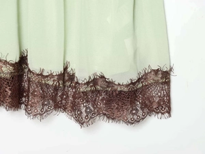 Detailed macro view of light green fabric hem with brown eyelash lace trim