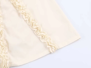 Detail van de crèmekleurige ruches en gelaagde plooien op deze zomerse midi-jurk
