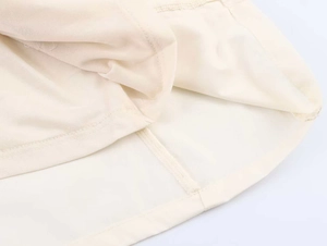Detailopname van de dubbellaagse zoom aan de beige midi-jurk met nette stiksels