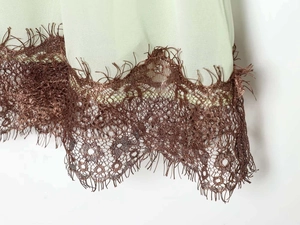 Close-up of sage green mini dress with brown floral lace hem and eyelash trim details