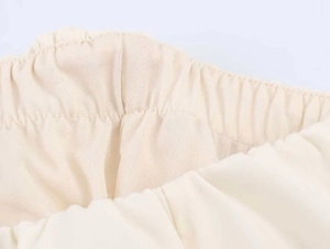 Detail van de elastische taille en fijne plooien op deze lichtbeige midi-jurk