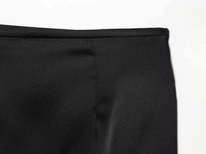 Détail de la taille d'une jupe en satin noir montrant les coutures fines et le tissu croisé