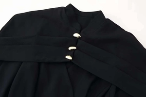 Detail of high collar black top featuring unique cross pleats and gold bean buttons