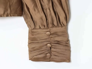 Detail von plissierten Ärmelbündchen mit Stoffknöpfen an einer bronzenen Satinbluse