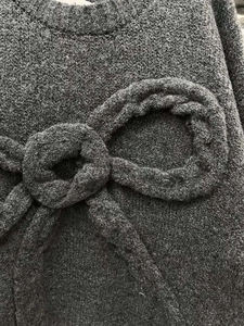 Gros plan d'un pull gris foncé en maille avec un grand nœud 3D et col rond élégant