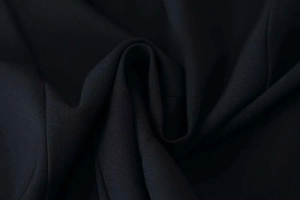 Macro shot of high-quality black twill fabric detailing the texture and drape of the coat