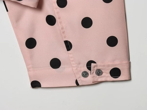 Close-up of pink polka dot fabric with glossy dark grey buttons and neat stitching