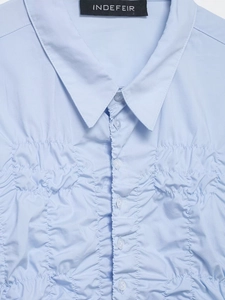 Detail of light blue poplin shirt featuring pleated texture and classic collar button-down