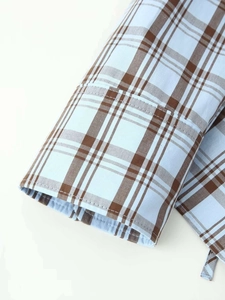 Détail des poignets de chemise en popeline à carreaux marron sur coton bleu clair doux