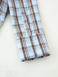 Gros plan du poignet d'une chemise à carreaux bleue avec boutons blancs et coton