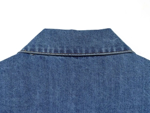 Gros plan des doubles surpiqûres et de la texture sergé sur un col de chemise en jean