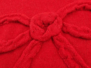 Gros plan sur la maille torsadée et le nœud 3D d'un pull rouge à col rond