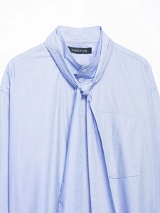 Detail of light blue shirt with tie neckline and INDEFEIR brand label on inner collar