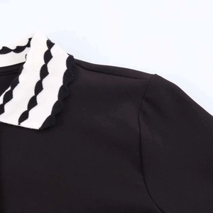 Detail of a black polo top featuring a unique white wavy edge collar and shoulder seams