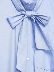 Detail of light blue shirt featuring a large bow-tie neckline and white buttons