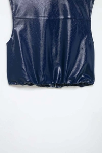 Dettaglio macro del gilet in pelle blu navy lucida con cerniera e bottoni metallici