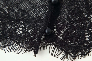 Detail of black eyelash lace fabric featuring delicate floral patterns and pearl buttons