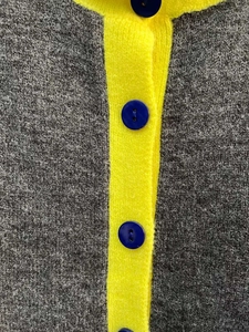 Dettaglio del cardigan grigio in maglia con bordo giallo e bottoni blu scuro
