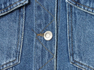 Close-up of vintage wash denim jacket showing silver metal button and yellow contrast stitching