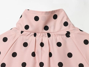 Detail of pink blouse with black polka dots, featuring a stand-up collar and pleated stitching