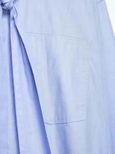 Detailed close-up of light blue shirt featuring a bow-tie neckline and textured fabric