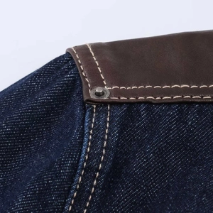 Détail de veste en jean avec patchwork de cuir marron et surpiqûres blanches