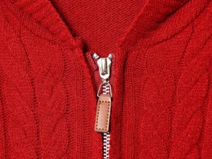Detail of red cable knit sweater showing silver metal zipper and brown leather puller