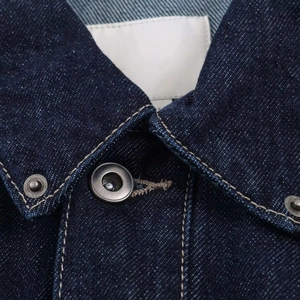 Détail du col d'une veste en jean bleu foncé avec surpiqûres et bouton en métal vintage