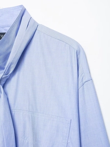 Detail of light blue shirt featuring a turnover collar and asymmetric bow tie design