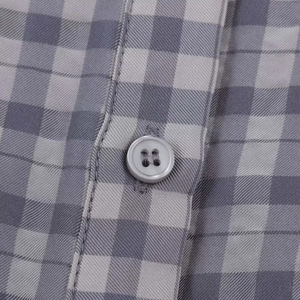Detailed macro view of gray plaid fabric texture and premium four-hole button stitching