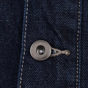 Détail du tissu denim bleu foncé montrant les boutons métalliques et les coutures